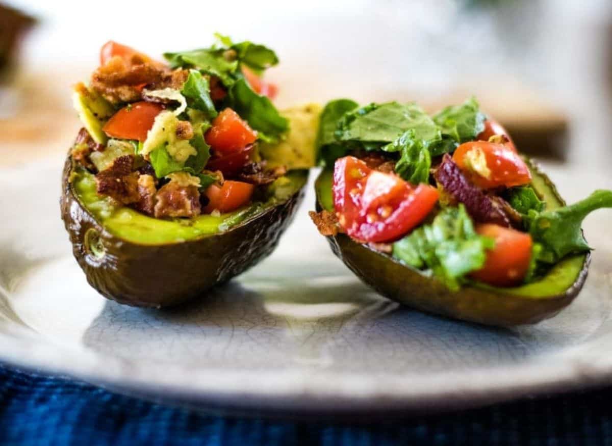 Stuffed and baked avocados on a wood board.