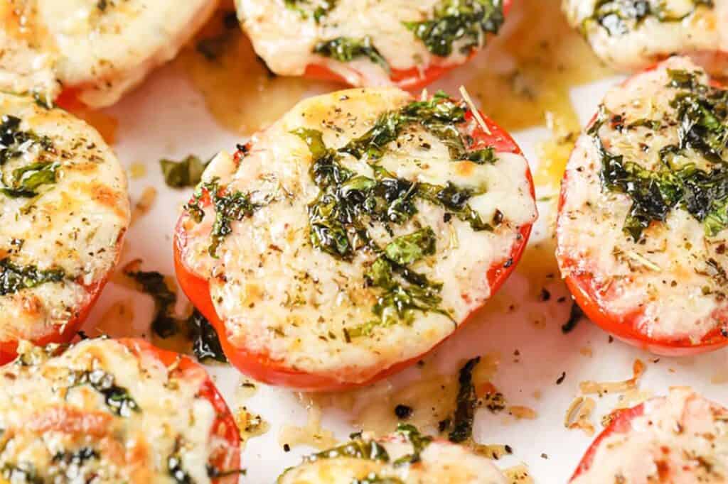Tomatoes topped with cheese and herbs on a white plate.