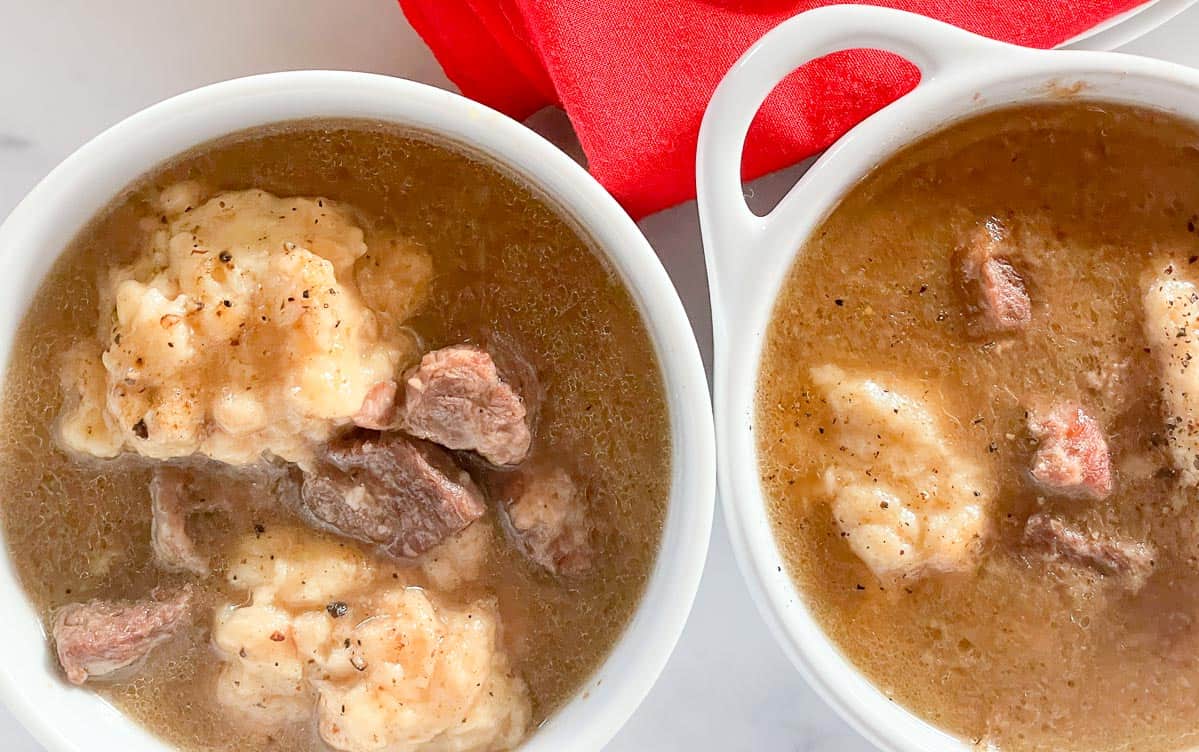 Beef and dumplings in a broth in two white bowls.