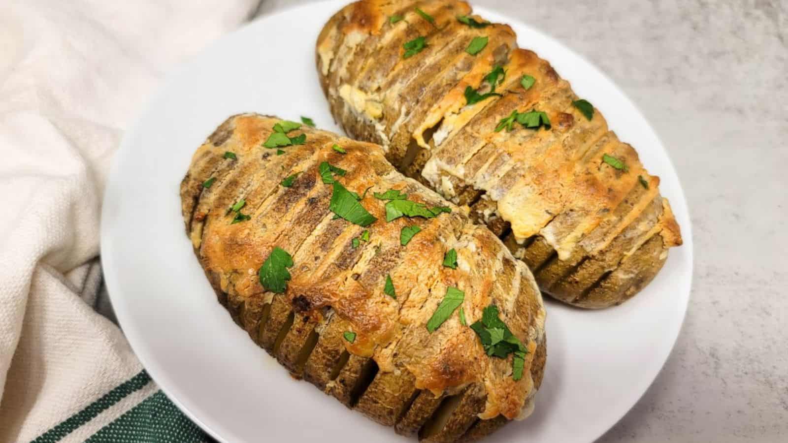 A white plate with two hasselback russet potatoes ready to eat.
