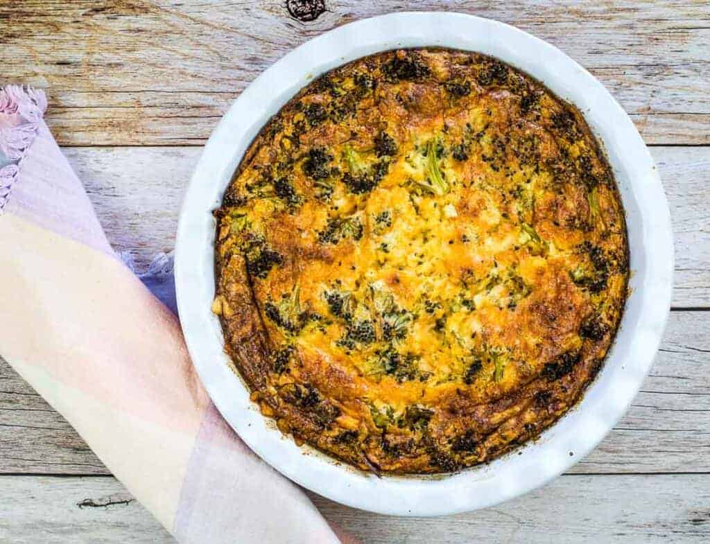 A slice of Broccoli 3-Cheese Impossible Quiche on a plate next to a glass of orange juice.