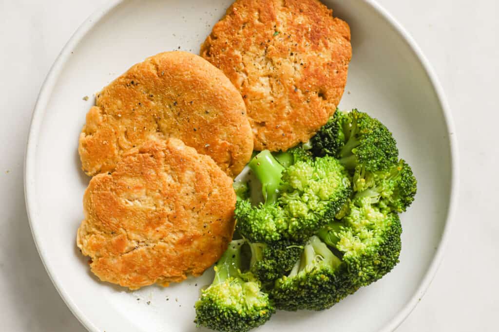 A white plate with broccoli and chicken patties.