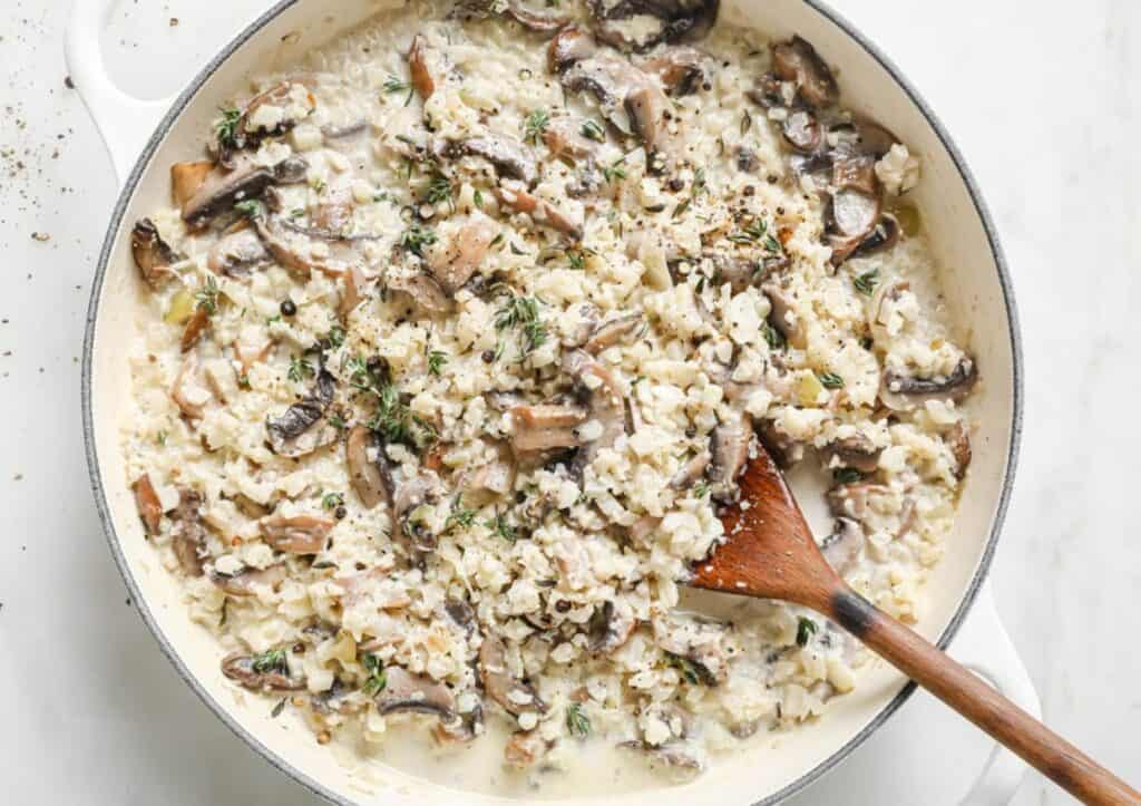 Cauliflower mushroom risotto in a pan with a wooden spoon.