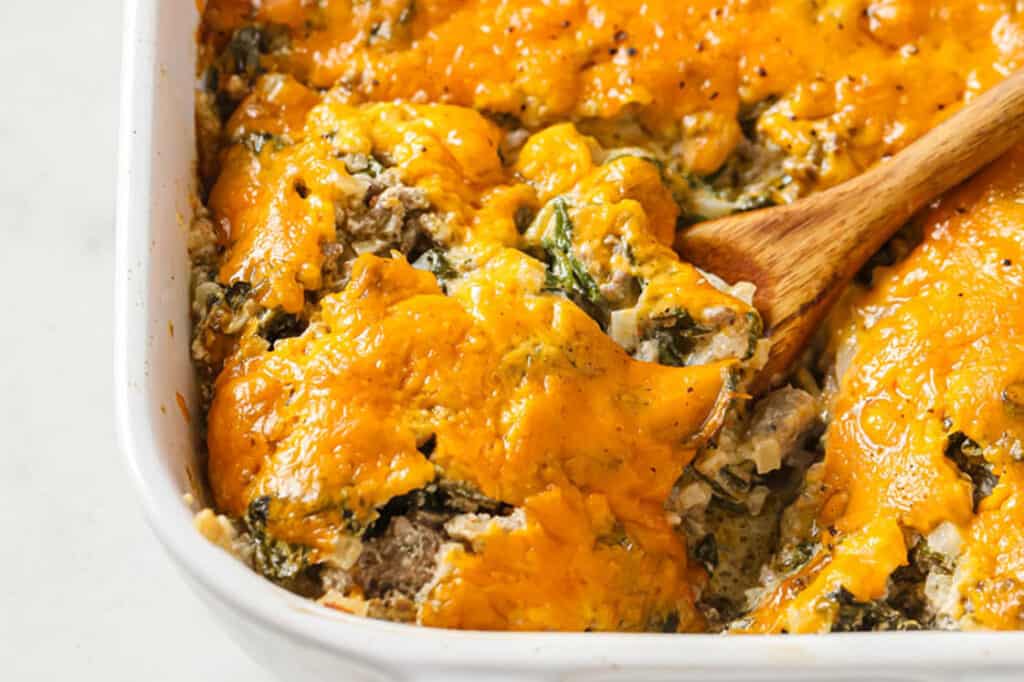 Cheesy spinach and sausage casserole with a wooden spoon.