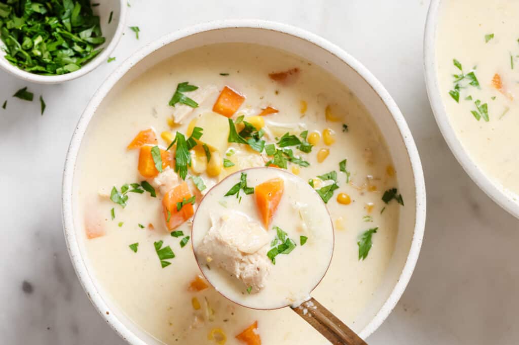 A bowl of chicken corn soup with carrots and parsley.