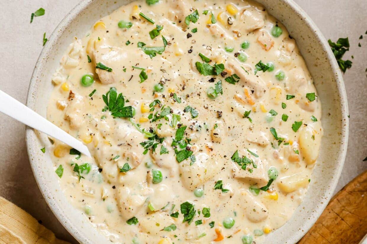 Chicken pot pie soup in a white bowl with a spoon.