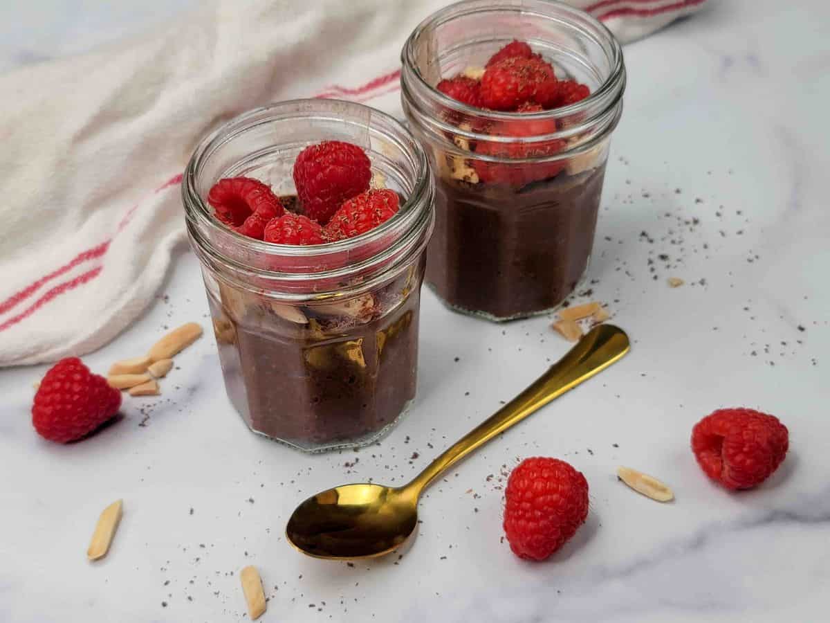 Two mason jars of chocolate chia seed pudding topped with raspberries.
