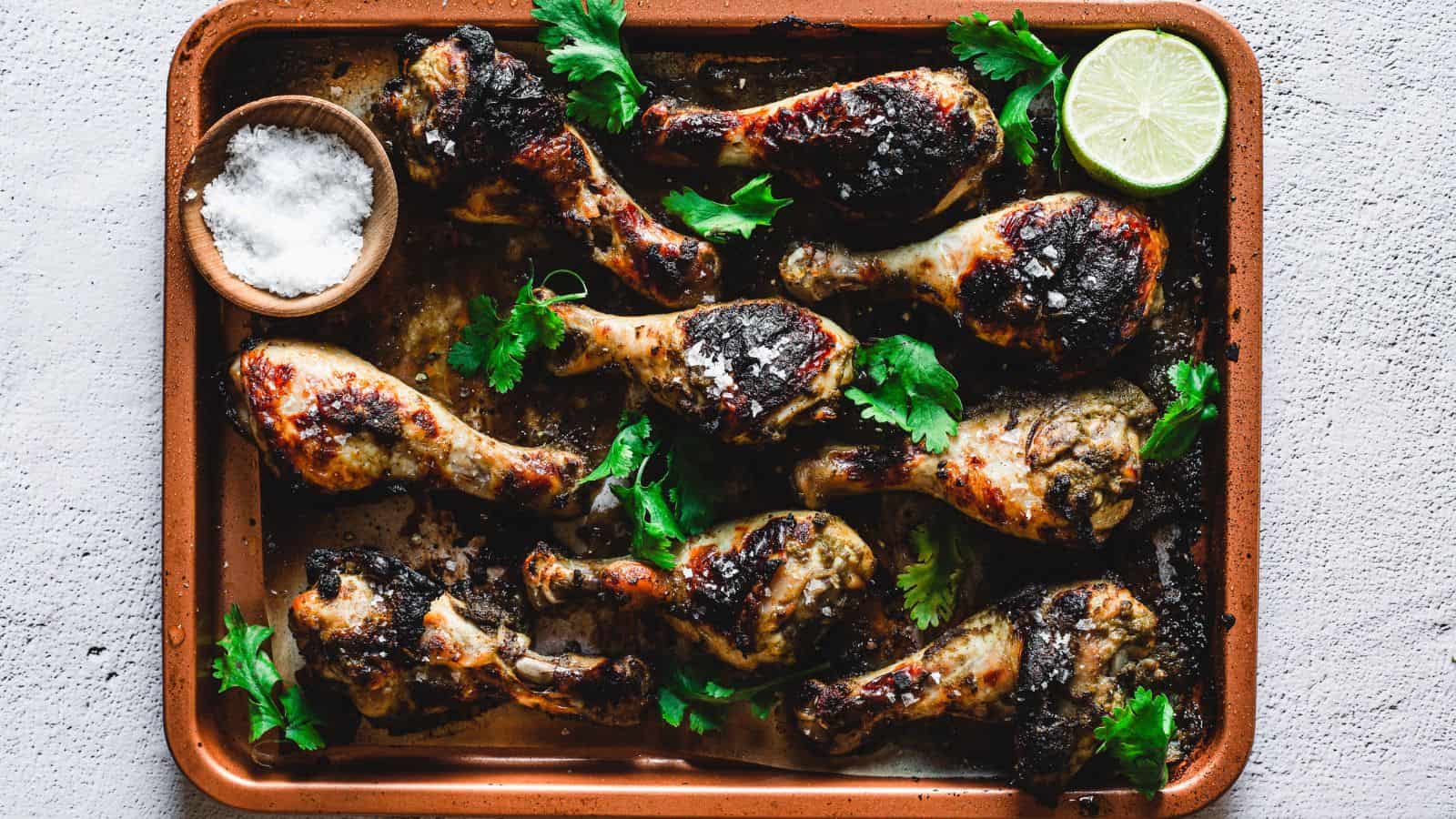 Grilled chicken legs on a brown tray with lime wedges.
