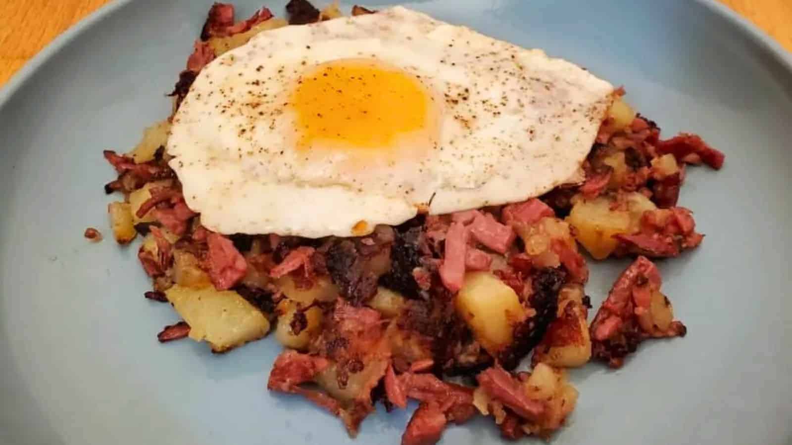 Image shows Corned Beef Hash with a fried egg on top in a blue plate.