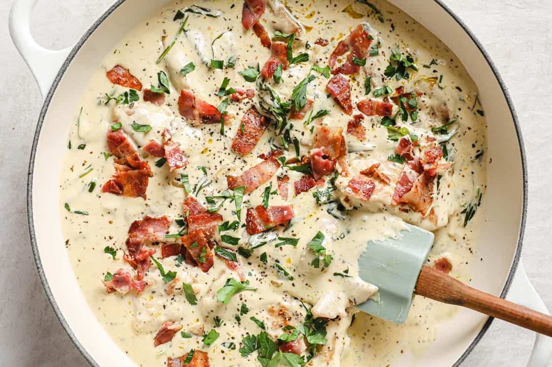 A pan of creamy dijon chicken with herbs and bacon.