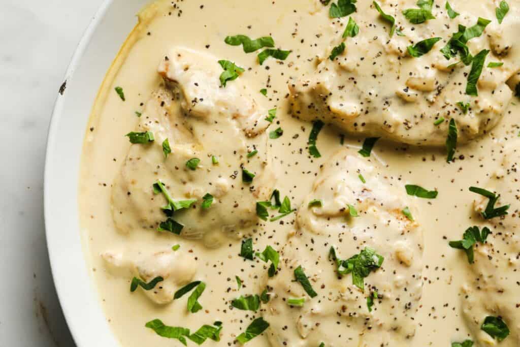 A white dish with chicken breasts in a creamy garlic sauce.