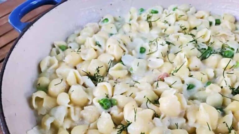 A pan full of pasta and peas on a wooden table.