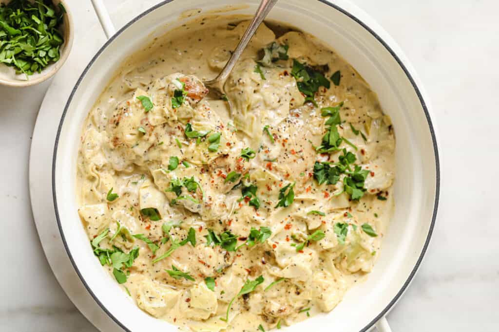 A pan filled with chicken in a creamy sauce with artichoke hearts.
