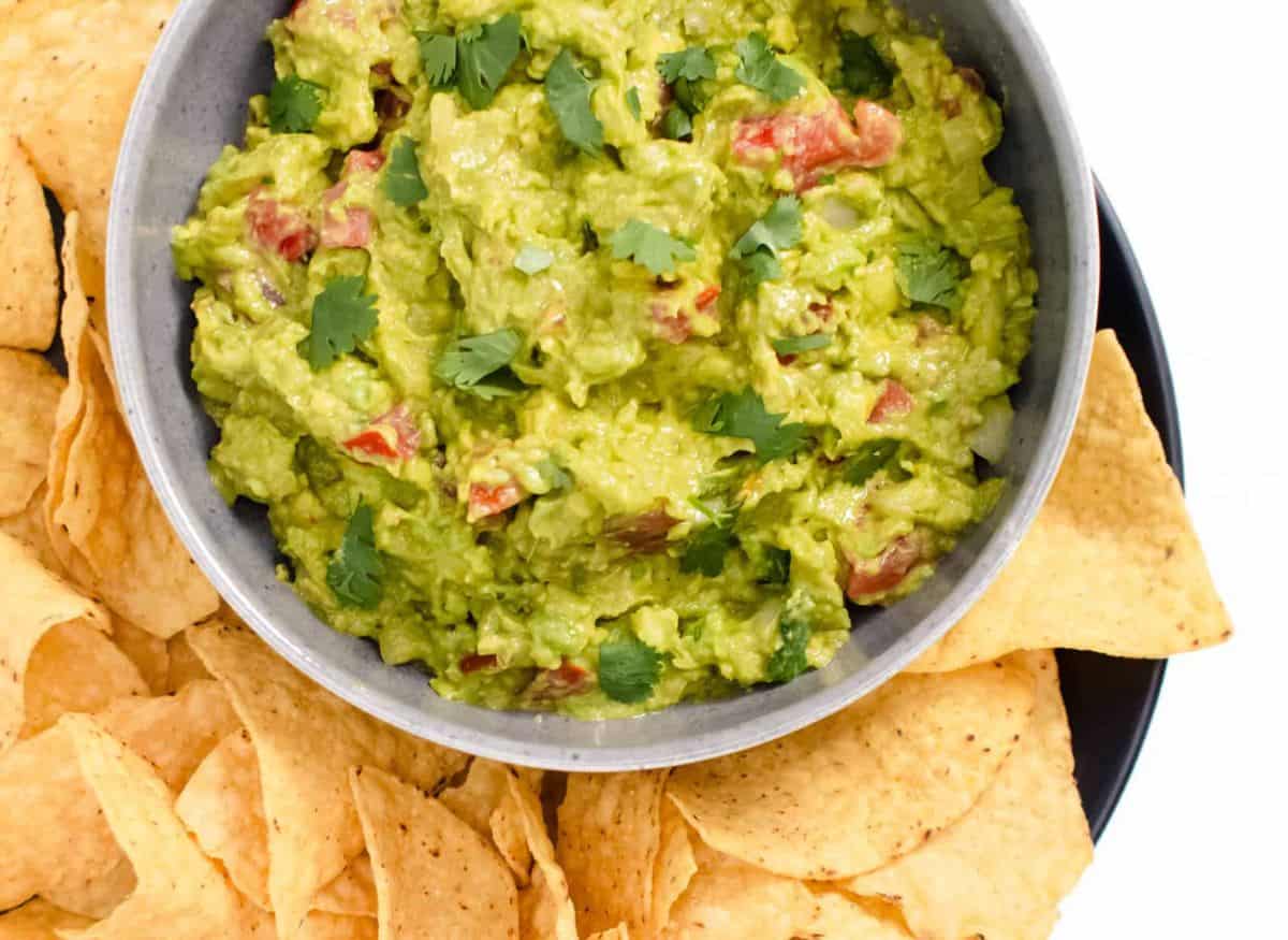 A bowl of guacamole and chips on a plate.