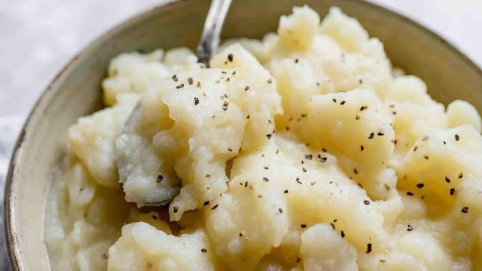 Close shot of a bowl of white stewed potatoes topped with black pepper.