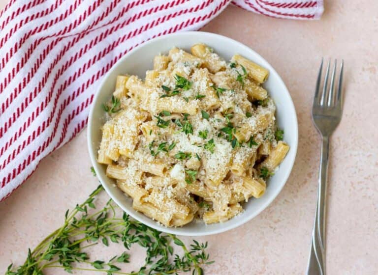 Pasta in a white bowl sprinkled with cheese and fresh herb.