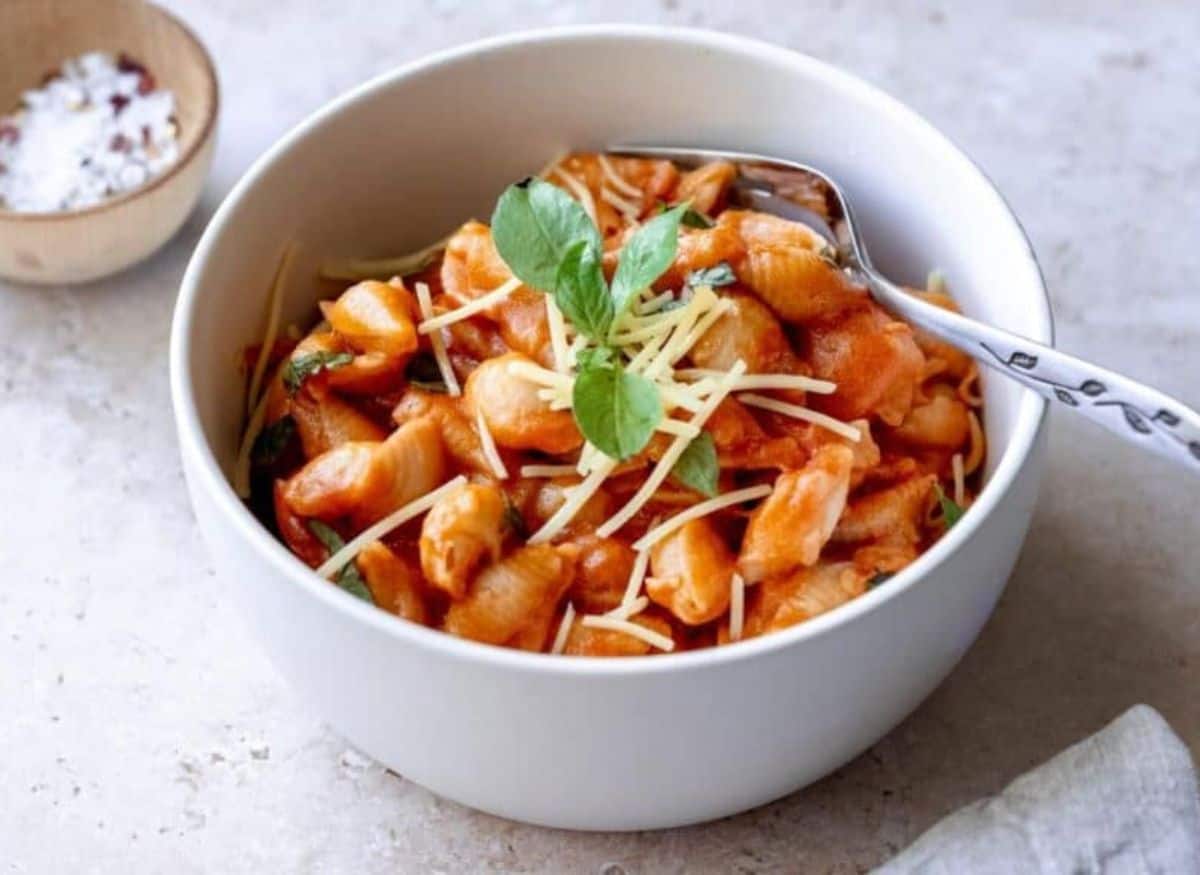 A white bowl filled with a red pasta topped with cheese and herbs.