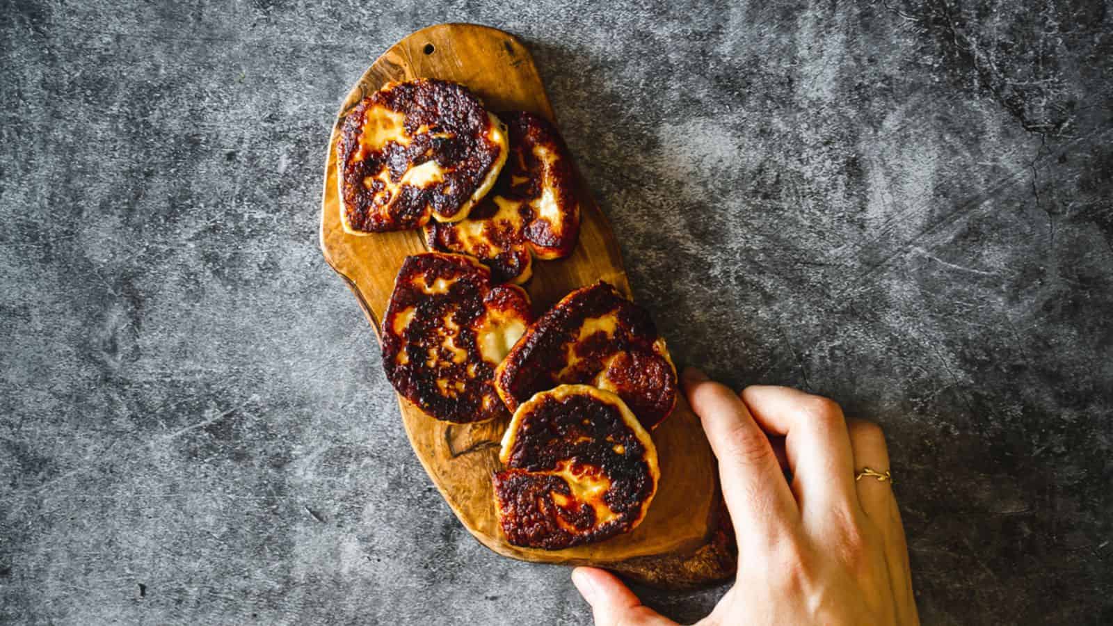 A person holding a wooden cutting board with roasted tomatoes on it.