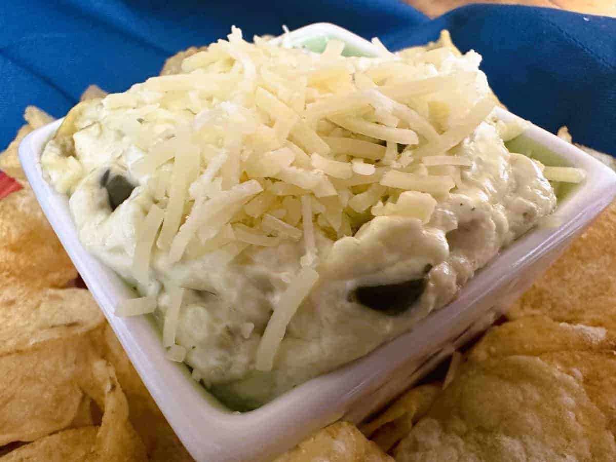 A white bowl of dip with chips and cheese.