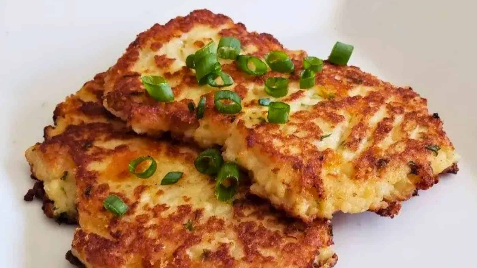 Image shows A plate of loaded mashed potato pancakes with green onions on it.