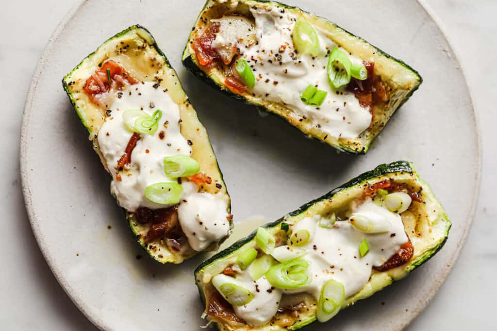 Three zucchini boats with cheese and green onions on a plate.