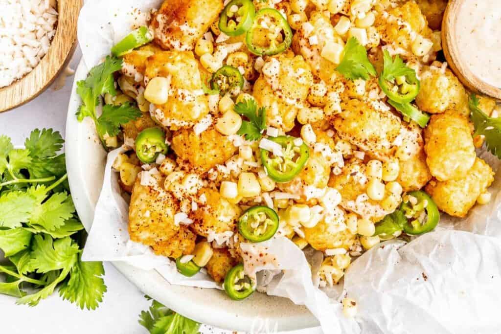 Mexican street corn over tater tots in a white bowl.