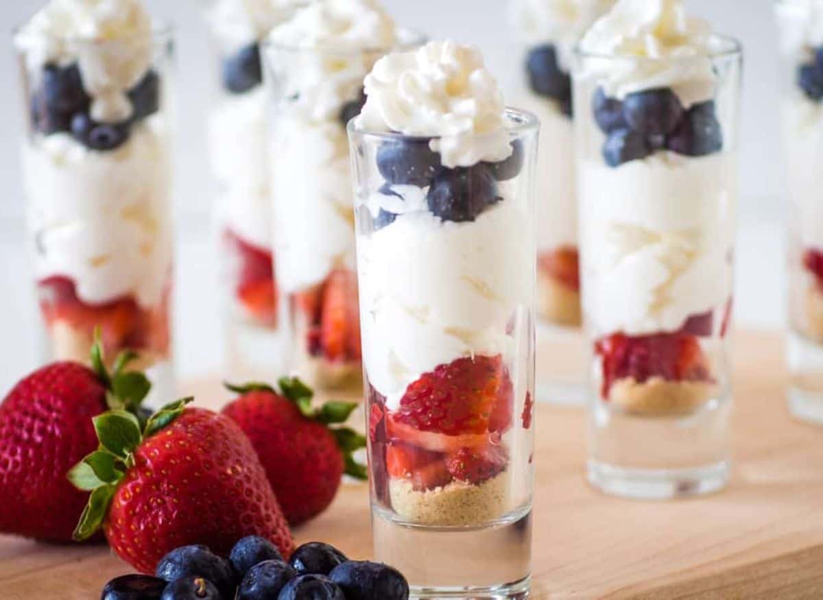 Cheesecake parfaits in shot glasses with blueberries and strawberries for a red white and blue dessert.