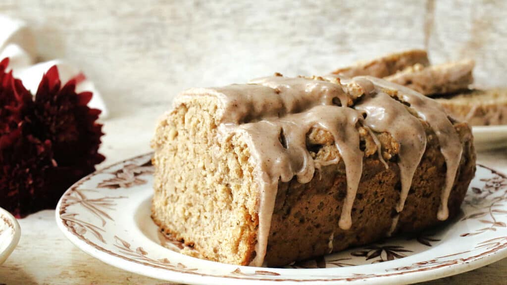 A slice of apple cider bread with icing on a plate.