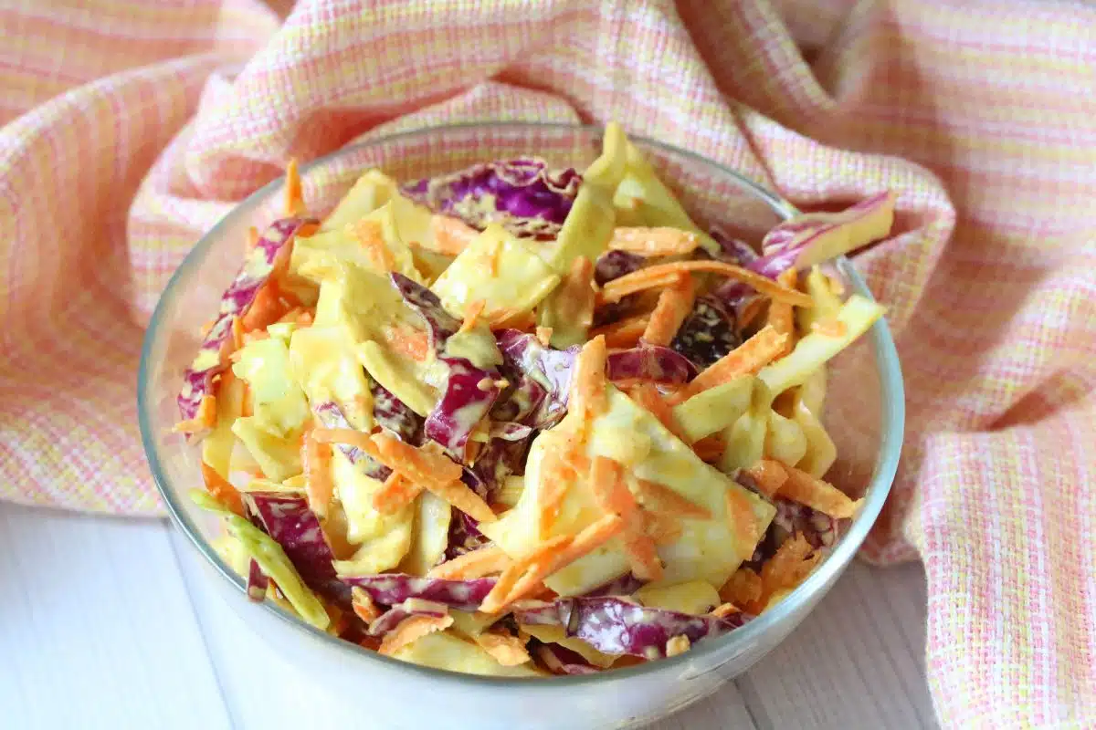 Dairy-free coleslaw in a glass bowl with a peach linen behind it.