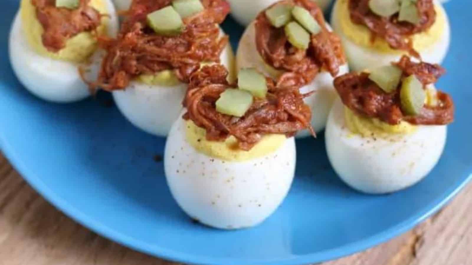 Blue plate with pulled pork deviled eggs, all topped with a pickle.