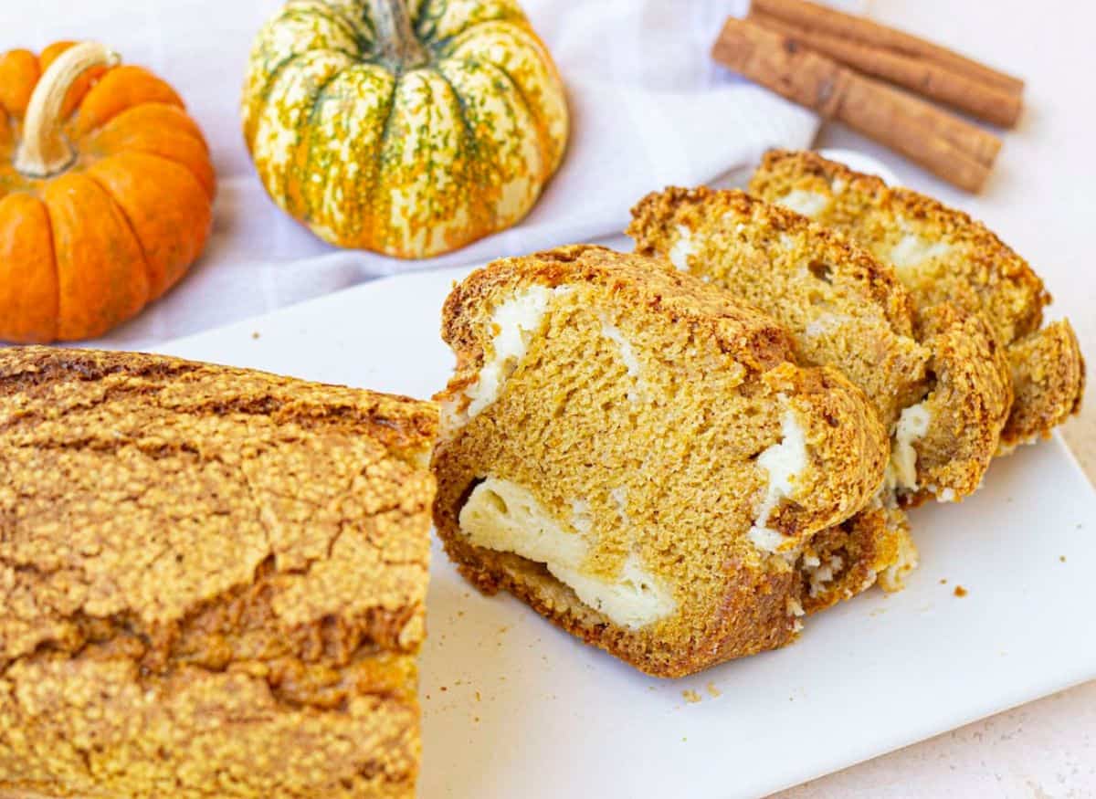Slices of pumpkin bread with cream cheese on a white board.