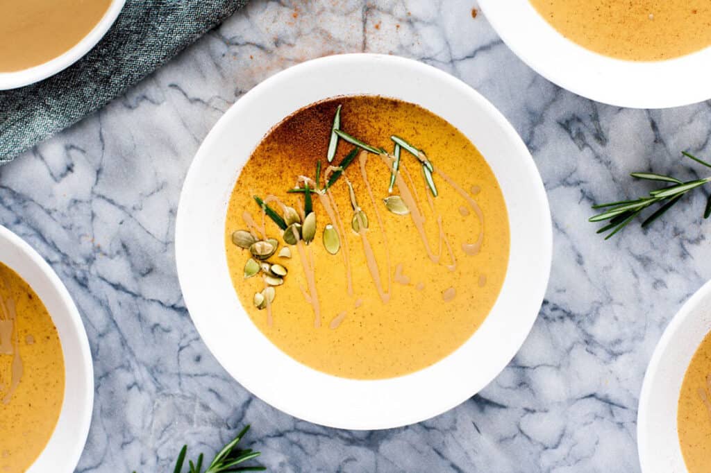 Four bowls of pumpkin soup with sprigs of rosemary.