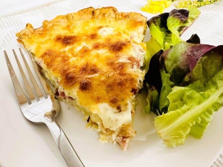 A slice of quiche on a plate with lettuce and a fork.