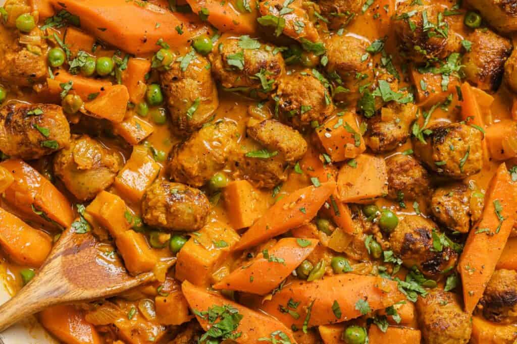 A dish with sausage, carrots and peas in it.