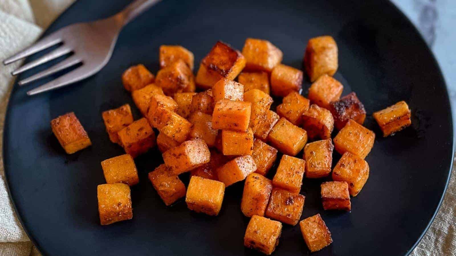 Sautéed sweet potatoes are shown on a black plate with the tines of a fork and a cream-colored linen.