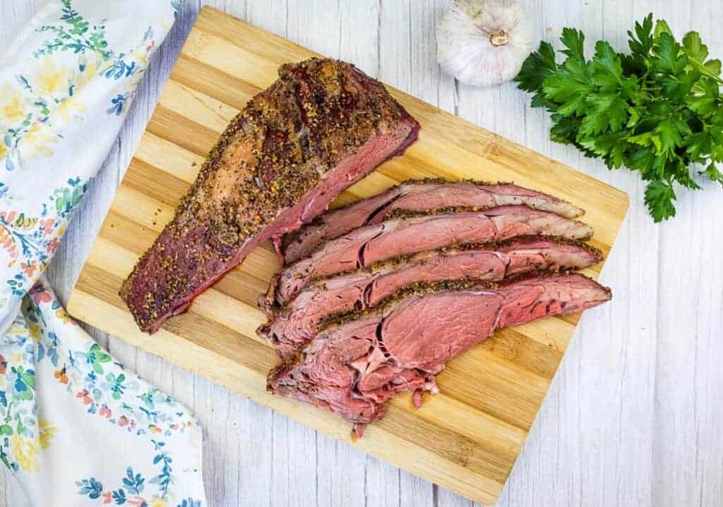 Sliced smoked ribeye beef on a cutting board.
