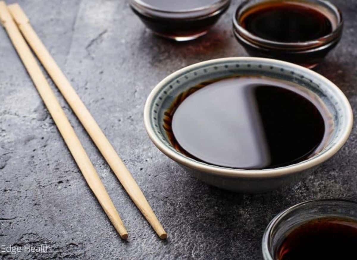 Small bowls of soy sauce with wooden chopsticks on dark background.