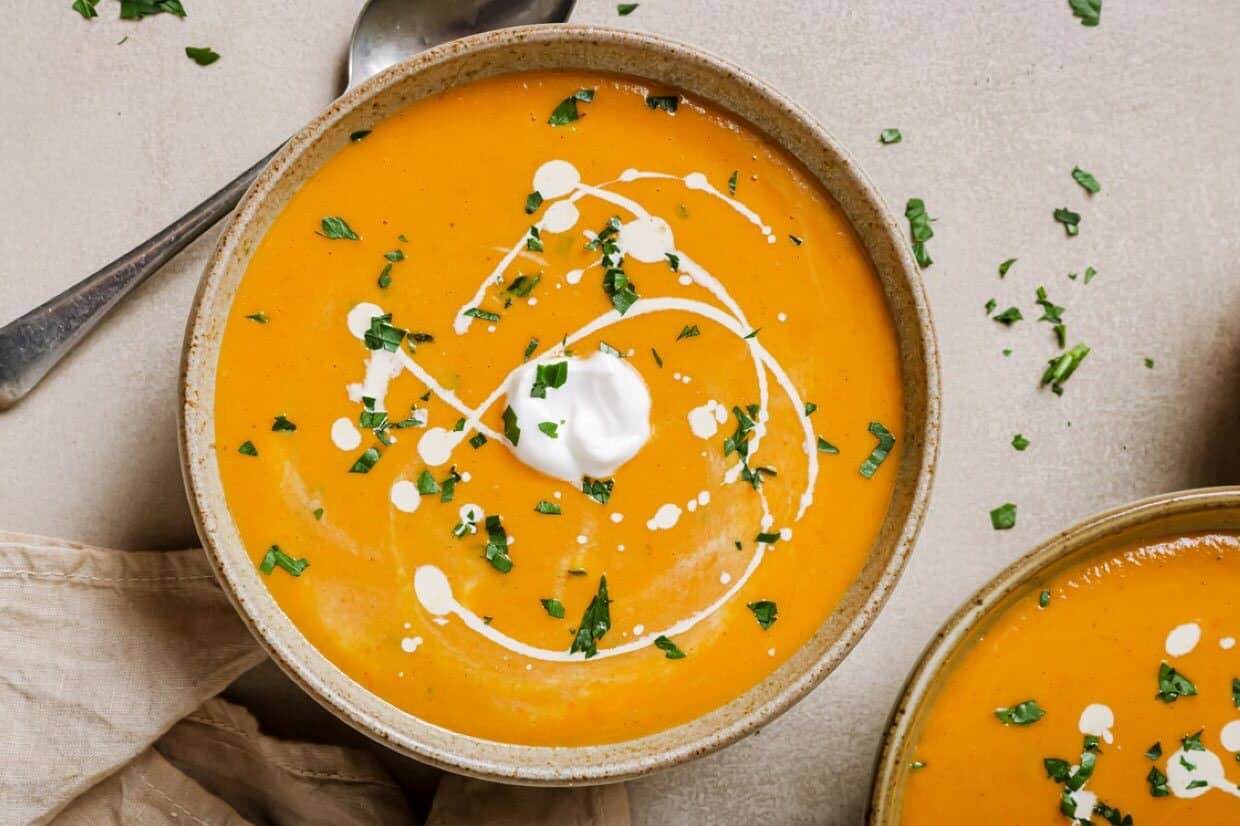 Two bowls of sweet potato and red pepper soup with sour cream and parsley.