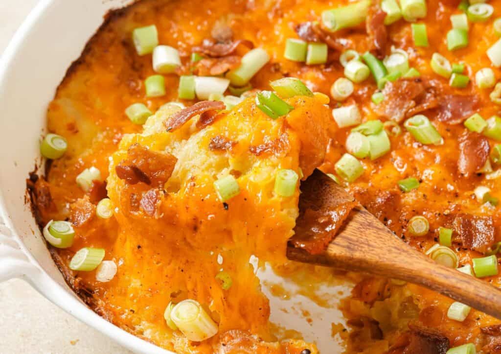 Cheesy twice baked potato casserole in a white dish with a wooden spoon.