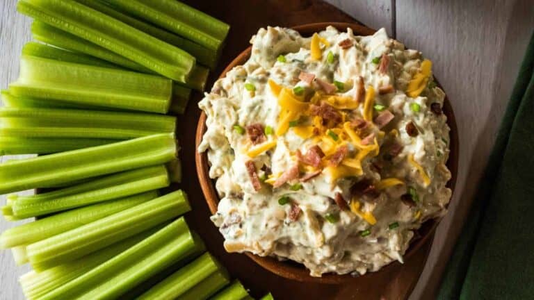 A bowl of bacon cheddar dip with celery sticks and cheese.