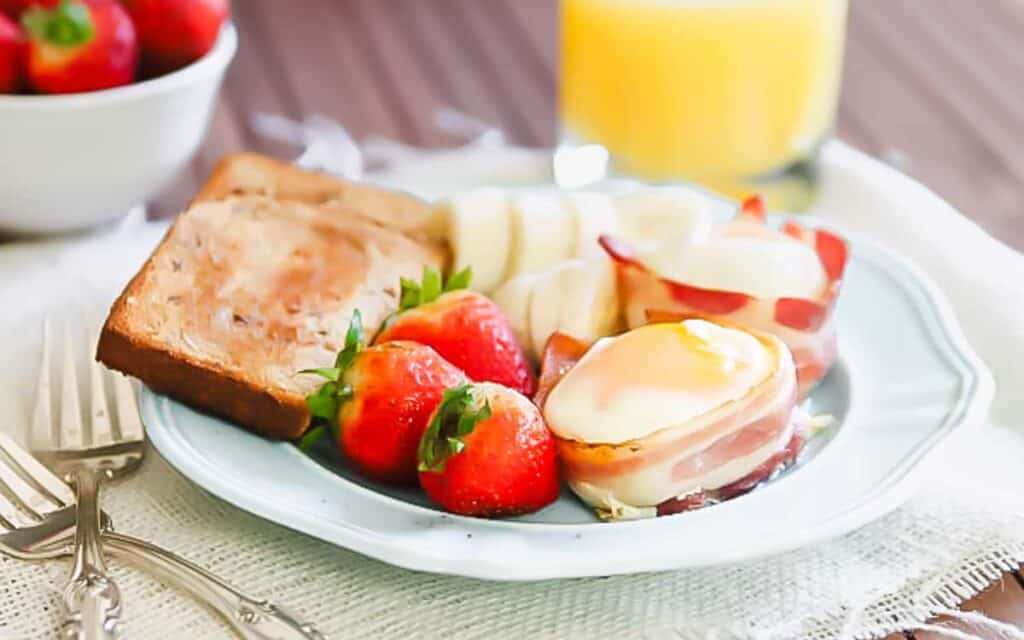 A plate of breakfast with eggs, bacon, toast, strawberries and orange juice.