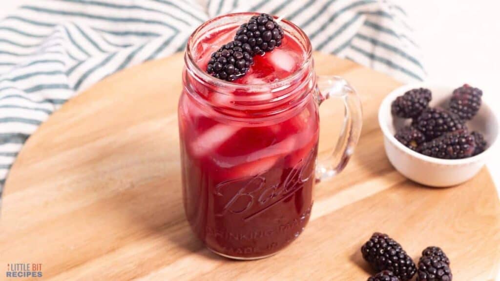 A mason jar filled with blackberries and ice tea.