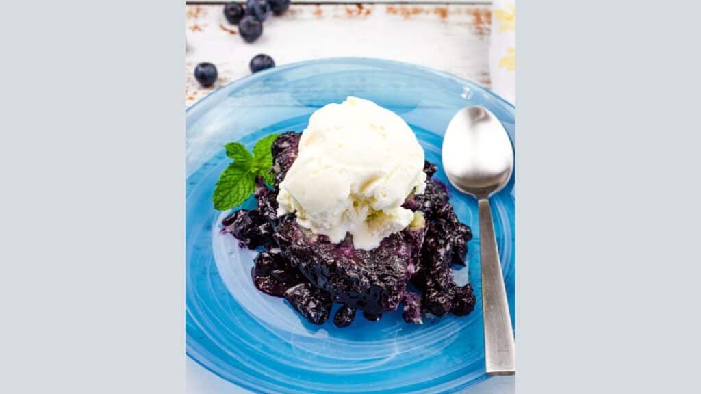 Blueberry Grunt with ice cream served on a vibrant blue plate, bringing you desserts to brighten your day.