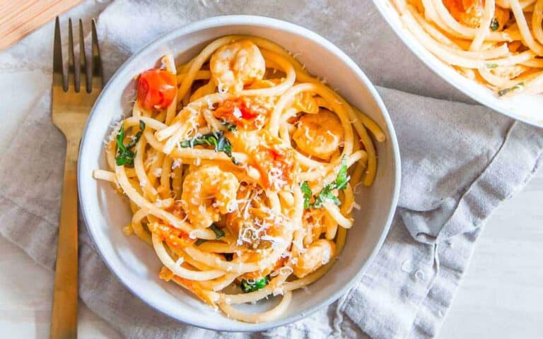 A bowl of pasta with shrimp and tomatoes.