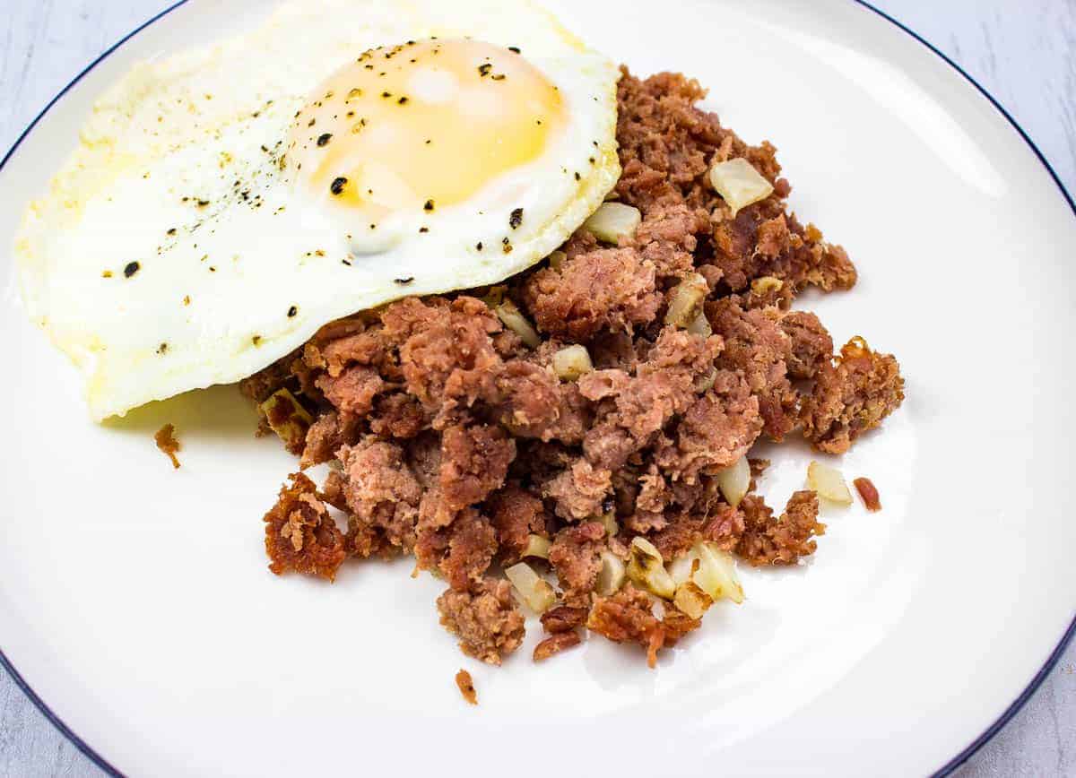 Canned corned beef hash on a plate with a fried egg.