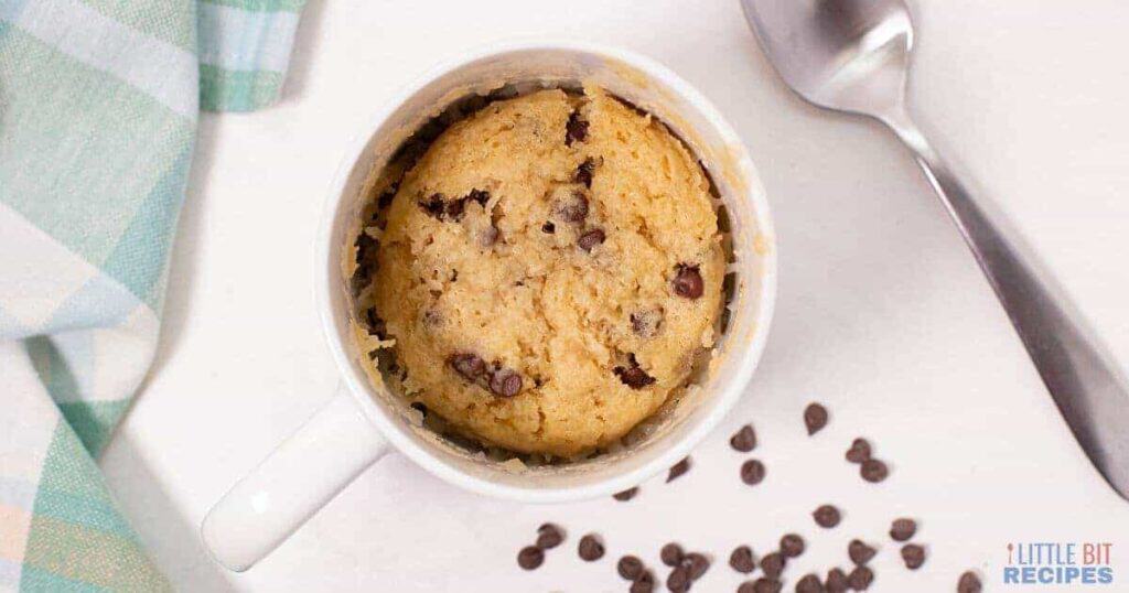 A chocolate chip cookie in a mug with a spoon.