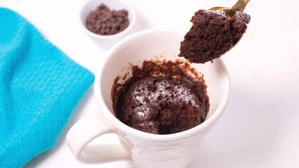 A chocolate cake in a mug with a spoon.