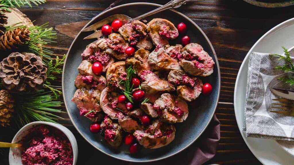 A plate of meat with cranberries and pine cones on a table.