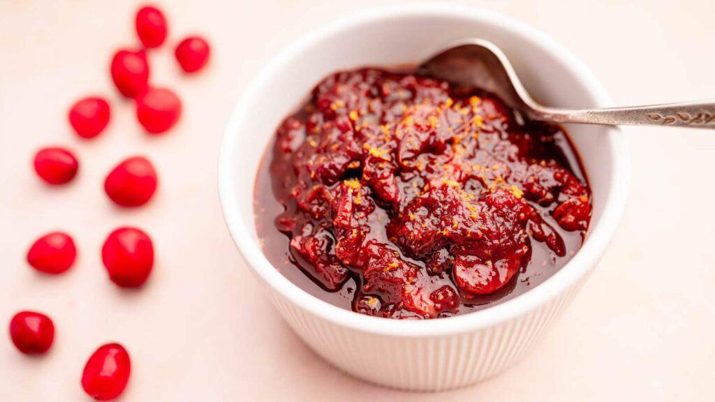 A bowl of cranberry sauce, a condiment for Thanksgiving, with a spoon.