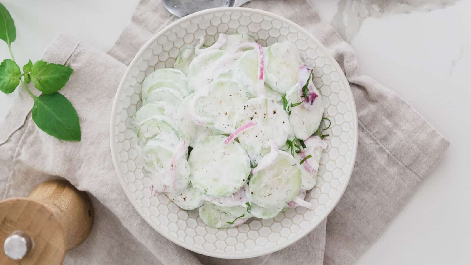Creamy cucumber salad with pickled red onions in a white textured bowl.